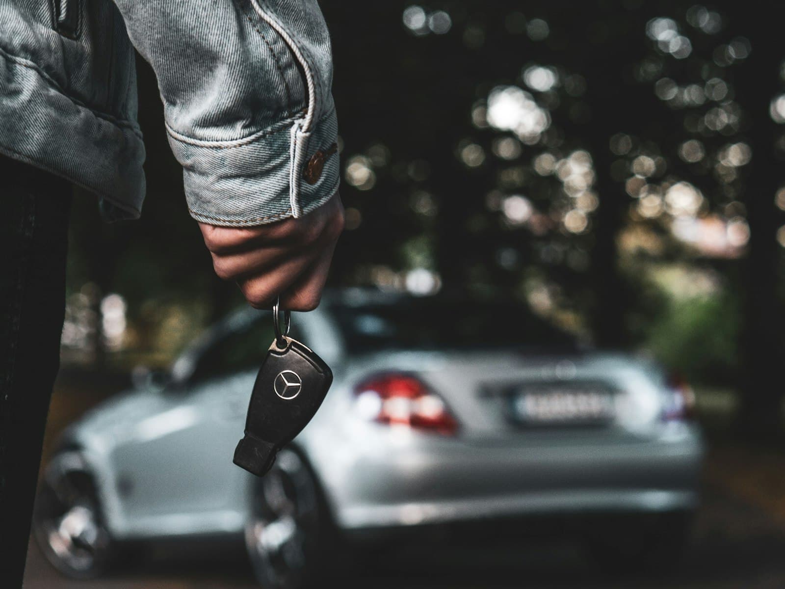 Person holding a set of car keys in front of a parked vehicle