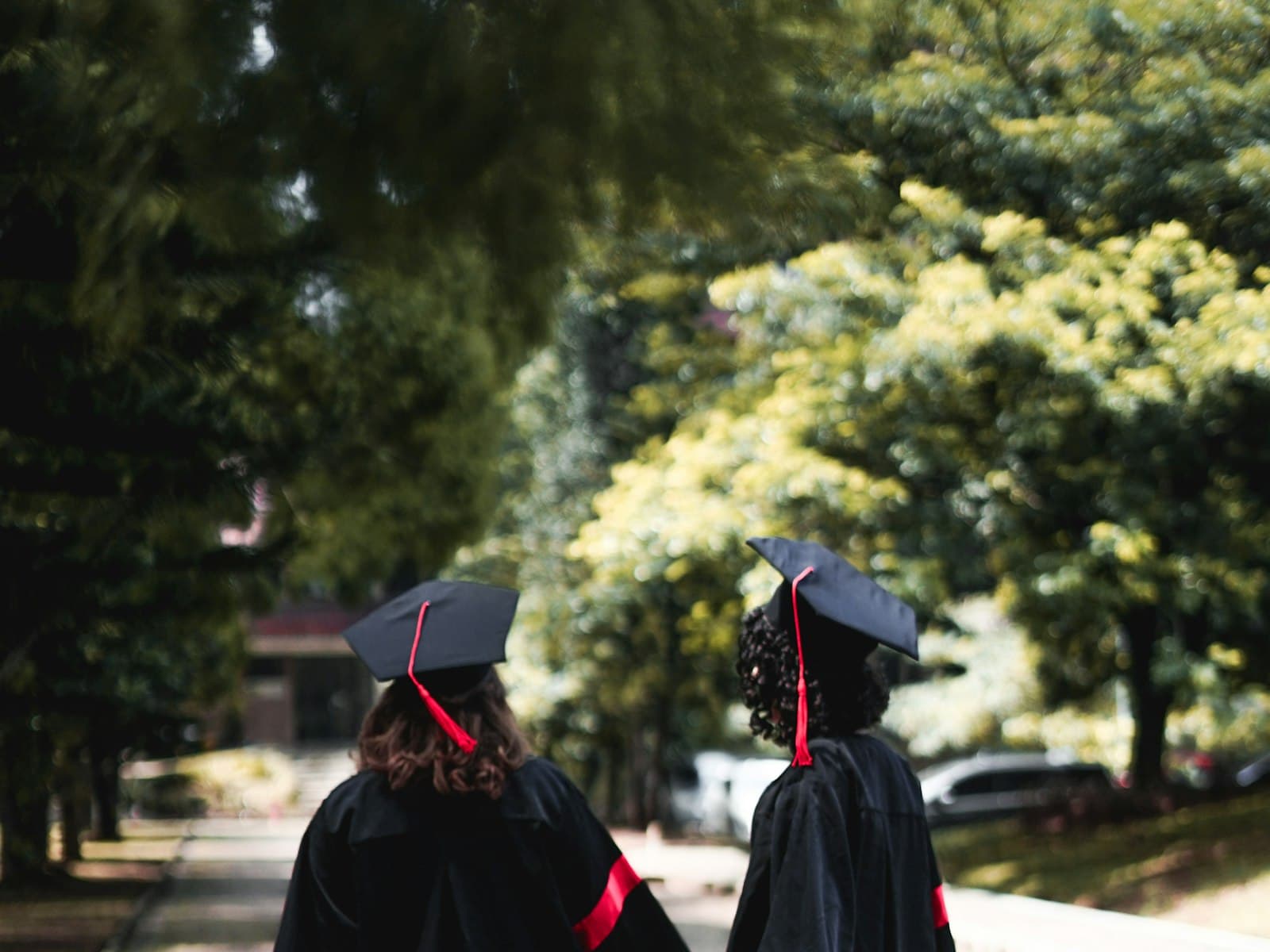 Two graduates in caps and gowns walking across a university campus